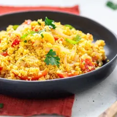 Un piatto invitante di cous cous freddo con pomodorini, cipolle e prezzemolo fresco. Perfetto per un pasto leggero e saporito.