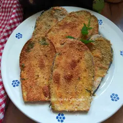 Fette dorate di cotoletta di melanzane impanate, guarnite con menta fresca, su un piatto bianco con decori blu.