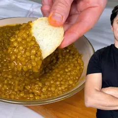 Un uomo sorride mentre un pezzo di pane intinge un piatto di saporite lenticchie in umido.
