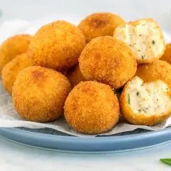 Un piatto di polpette di ricotta dorate e croccanti, alcune intere, altre spezzate per mostrare il ripieno morbido e profumato.