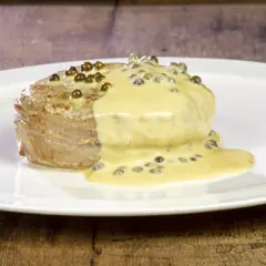 Un succulento filetto al pepe verde, nappato da una cremosa salsa, adagiato su un piatto bianco.