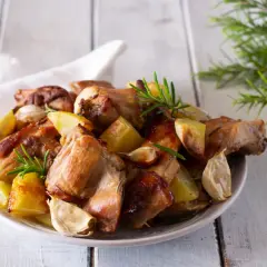 Piatto invitante di coniglio al forno con patate arrosto, aglio e rosmarino su un tavolo di legno.