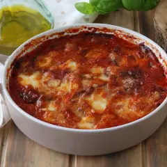 Parmigiana di melanzane appena sfornata, dorata e filante, con pomodoro e basilico fresco.