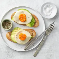 Due fette di pane tostato con avocado, formaggio e un occhio di bue, condite con pepe.
