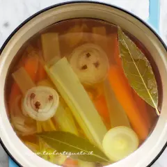Brodo vegetale ricetta: carote, sedano, cipolla con chiodi di garofano e alloro in pentola.