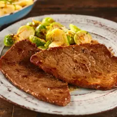 Due fette di paillard di vitello succulento, servite con cavolini di Bruxelles arrostiti e un contorno di pasta in una padella.