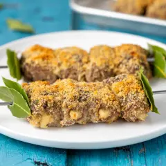 Braciole alla messinese su spiedini, impanate e dorate, guarnite con foglie di alloro.