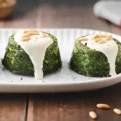 Delizioso flan di verdure servito su un piatto bianco, guarnito con salsa cremosa e pinoli tostati.