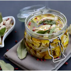 Tonno di coniglio sott'olio, sfilacciato e conservato in un barattolo di vetro con erbe aromatiche e pepe rosa.