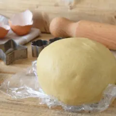 Impasto per crostata pronto, con stampini, uovo rotto e mattarello. La pasta frolla friabile per crostata è perfetta per dolci fatti in casa.