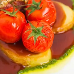 Pomodori alla griglia succosi su patate, immersi in una salsa scura e guarniti con un filo di pesto verde.