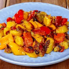 Pipi e patate arrostiti, un contorno colorato e saporito, servito su un piatto azzurro.