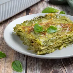 Una fetta di lasagne al pesto, stratificata e dorata, guarnita con basilico fresco su un piatto grigio.