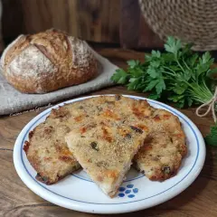 Frittata di pane dorata e saporita, servita su un piatto bianco con bordi blu, accanto a pane fresco e erbe aromatiche.