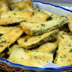 Fettine di zucchine impanate e dorate, appena tolte dalla padella, servite in una ciotola.