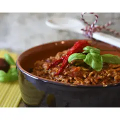 Un saporito ragù di verdure, guarnito con peperoncino e basilico, in una ciotola di terracotta.
