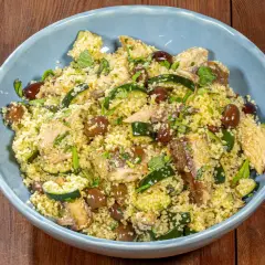 Un saporito cous cous con verdure, olive e pesce, guarnito con erbe fresche.