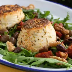 Due dischi di ricotta al forno su un letto di rucola, pomodori secchi, olive e noci.