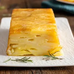Sformato di patate a fette dorato e invitante, servito su un piatto bianco con rametti di rosmarino.