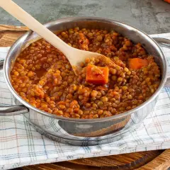 Un pentolino pieno di saporito ragù di lenticchie, con pezzi di carota e un cucchiaio di legno.