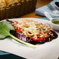 Caponata di melanzane gratinata con olive, pomodoro e formaggio fuso, servita con spinaci freschi e salsa verde.