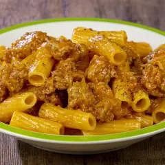 Piatto di rigatoni conditi con un ricco sugo di salsiccia, cosparso di pepe nero.