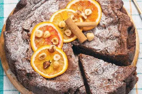 Deliziosa torta di pane al cioccolato, cosparsa di zucchero a velo, decorata con fette d'arancia, nocciole e cannella.