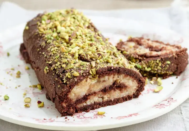 Rotolo al cioccolato e pistacchio, un dolce con farina di riso, ripieno di crema chiara e decorato con granella verde.