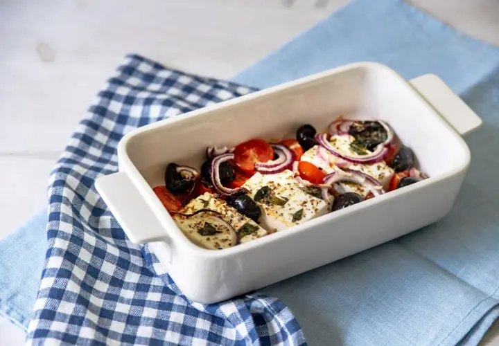 Feta al forno con pomodorini, olive nere e cipolla rossa, condita con erbe aromatiche.