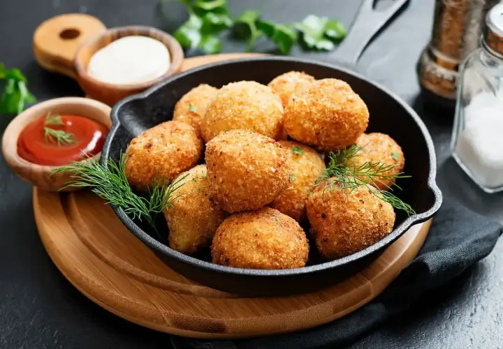 Croccanti polpette di zucca dorate servite in una padella di ghisa, con salse e erbe aromatiche.