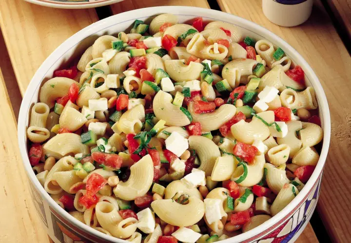 Un invitante piatto di pasta fredda con zucchine, pomodorini, cubetti di formaggio e fagioli, perfetto per un pasto estivo.