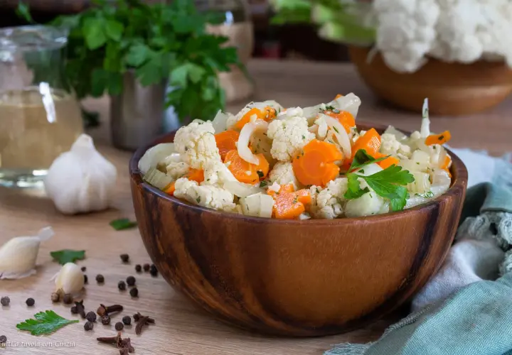 Una ciotola di legno piena di giardiniera fatta in casa, con cavolfiore, carote e cipolle, guarnita con prezzemolo fresco.