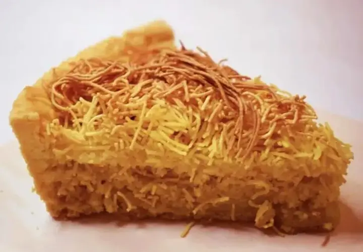 Una fetta di torta di tagliatelle, con la crosta dorata e un ripieno soffice, decorata con fili croccanti.