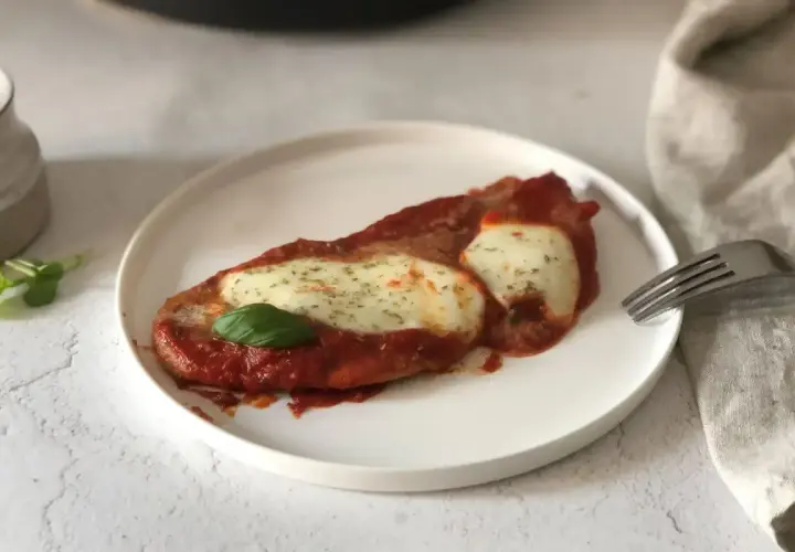 Scaloppine alla pizzaiola su un piatto bianco, con mozzarella filante, salsa di pomodoro e una foglia di basilico.