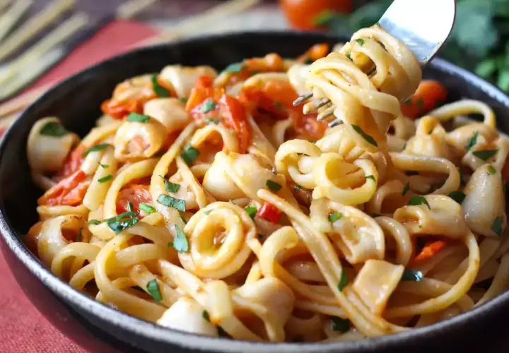 Un primo piatto invitante: pasta con calamari, pomodorini e prezzemolo fresco. Un boccone di mare su un piatto di pasta.