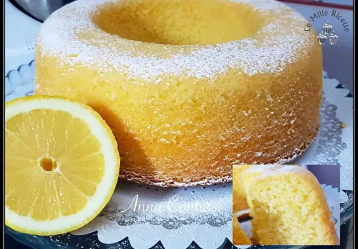 Un soffice ciambellone al limone, spolverato di zucchero a velo, accanto a una fetta di limone fresca.
