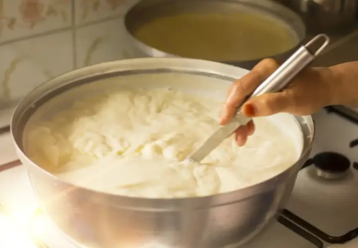 Mano che mescola un pentolone pieno di cremoso yogurt fatto in casa, pronto per essere gustato.