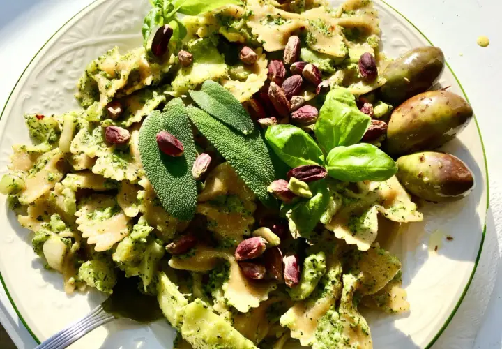 Farfalle condite con un cremoso pesto di salvia, guarnite con pistacchi, basilico e olive verdi.