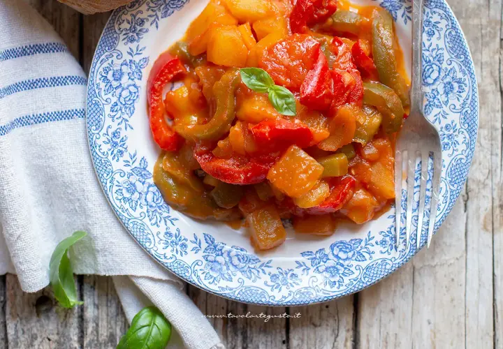 Un piatto di peperonata con patate, colorata e saporita, guarnita con basilico fresco.