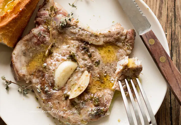 Succulente braciole di maiale cotte con aglio e erbe aromatiche, servite con pane croccante e un filo d'olio.