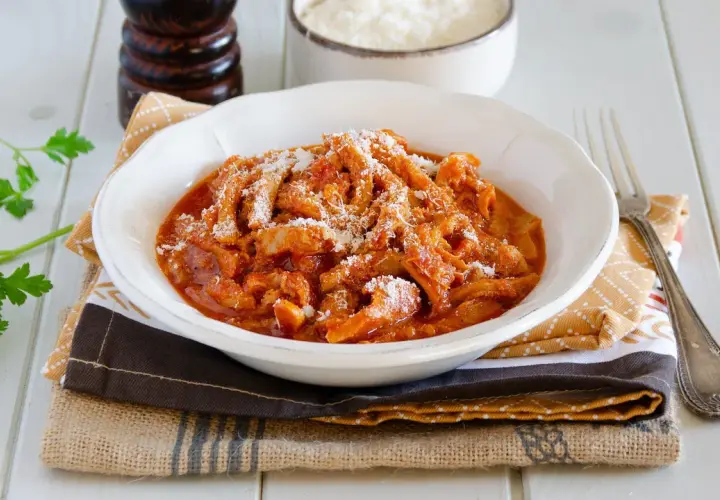 Un invitante piatto di trippa alla parmigiana, cosparso di formaggio grattugiato, pronto per essere gustato.