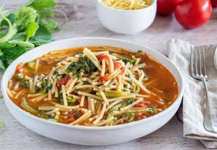 Un piatto fumante di pasta con i tenerumi, un classico siciliano, con pomodoro e verdure fresche.