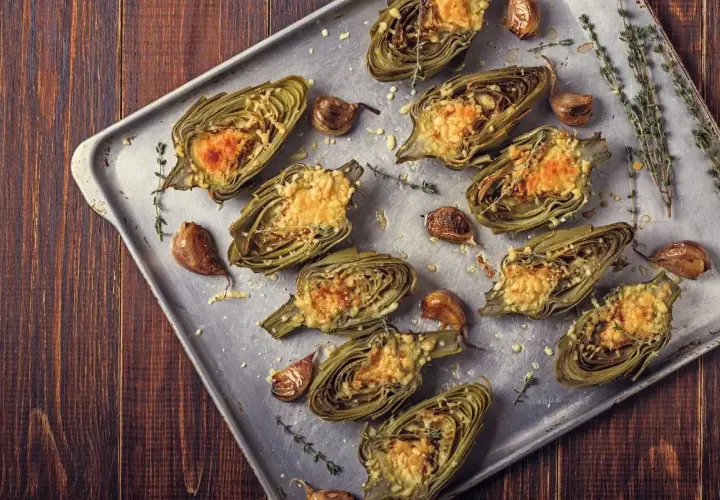 Carciofi al forno morbidi, ripieni e gratinati, con aglio e timo su teglia metallica.