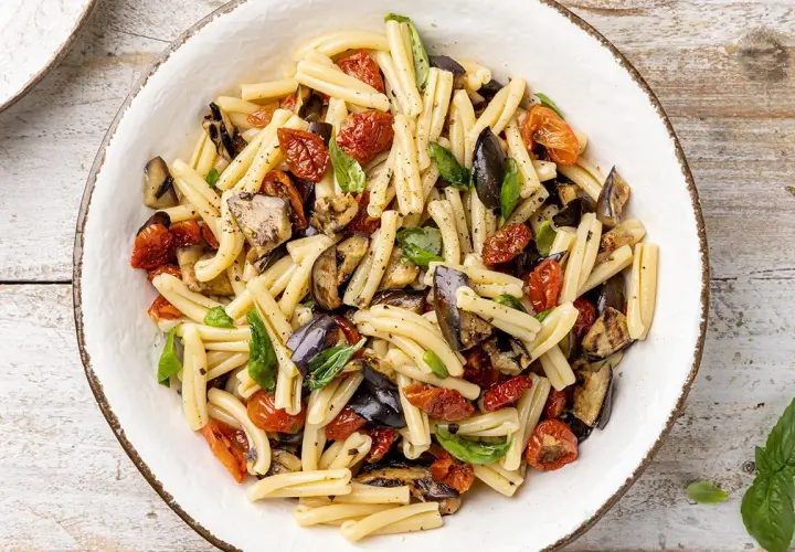 Pasta fredda con melanzane grigliate, pomodorini secchi e basilico fresco, un piatto estivo colorato e saporito.