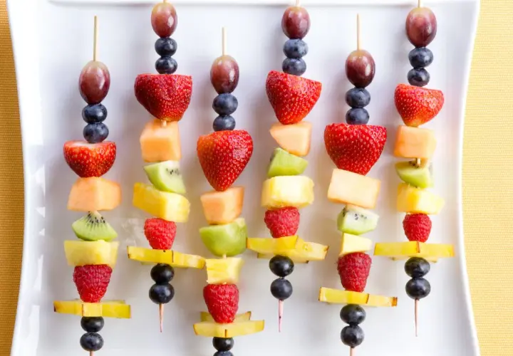 Spiedini di frutta colorati, perfetti per idee fresche e golose. Fragole, kiwi, melone e mirtilli su stecchini.