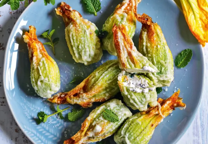 Fiori di zucca fritti, ripieni di formaggio cremoso e guarniti con menta fresca su un piatto blu.