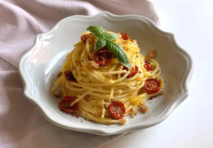 Un piatto di spaghetti conditi con pomodorini gialli secchi, basilico fresco e pangrattato croccante.