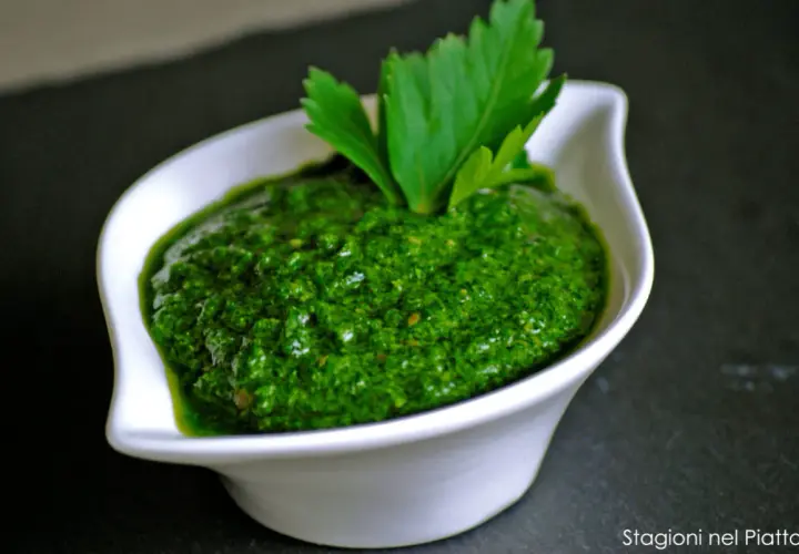 Una ciotola bianca contiene una vibrante ricetta salsa verde leggera, guarnita con prezzemolo fresco.