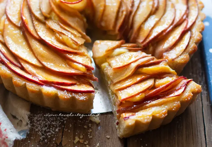 Una fetta di crostata di mele dorata, con mele caramellate disposte a rosa su una base friabile.