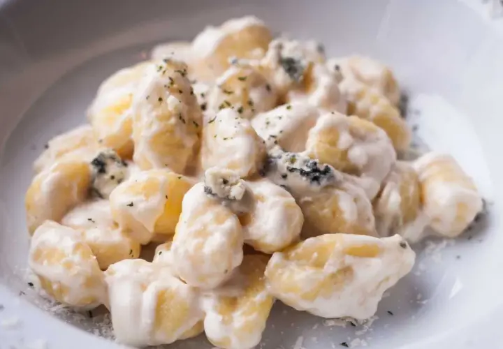 Gnocchi al gorgonzola cremosi, con pezzetti di formaggio blu e erbe aromatiche, serviti in un piatto bianco.